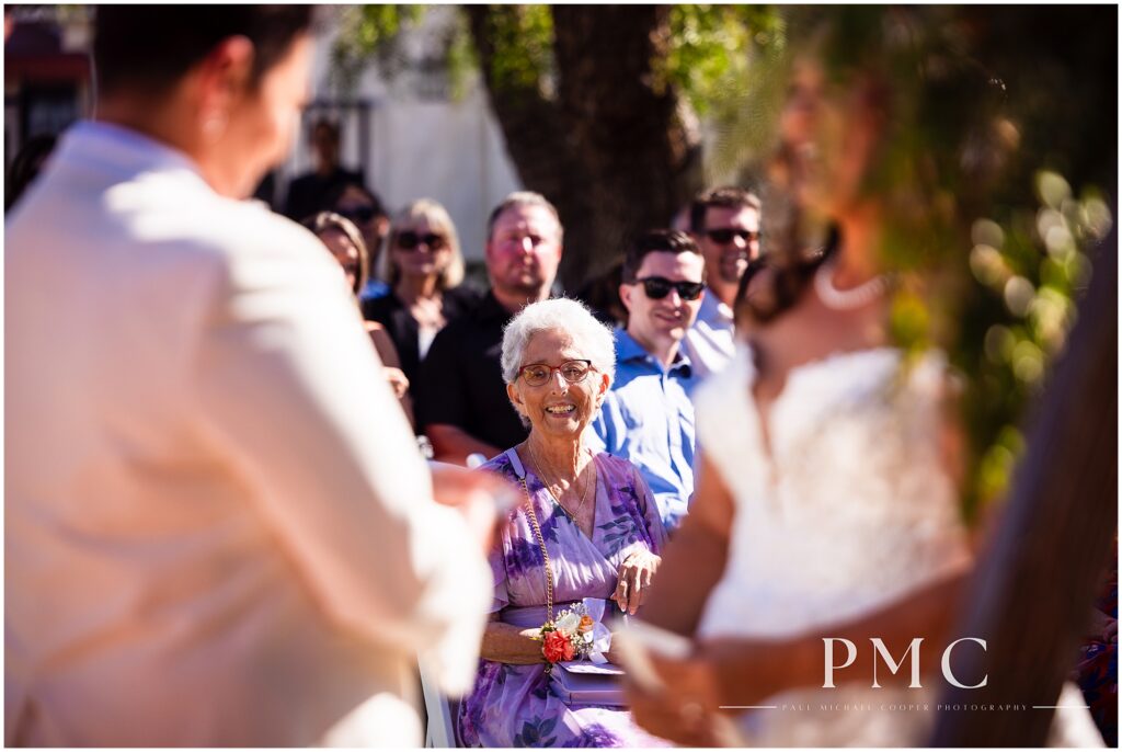 The mother of one of the brides smiles happily at the couple during their ceremony at the historical Rancho Minerva Wedding Venue in Vista.