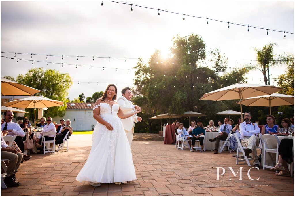 Two brides smile during their choreographed first dance on their summer wedding day at the terracotta Rancho Minerva Wedding Venue.