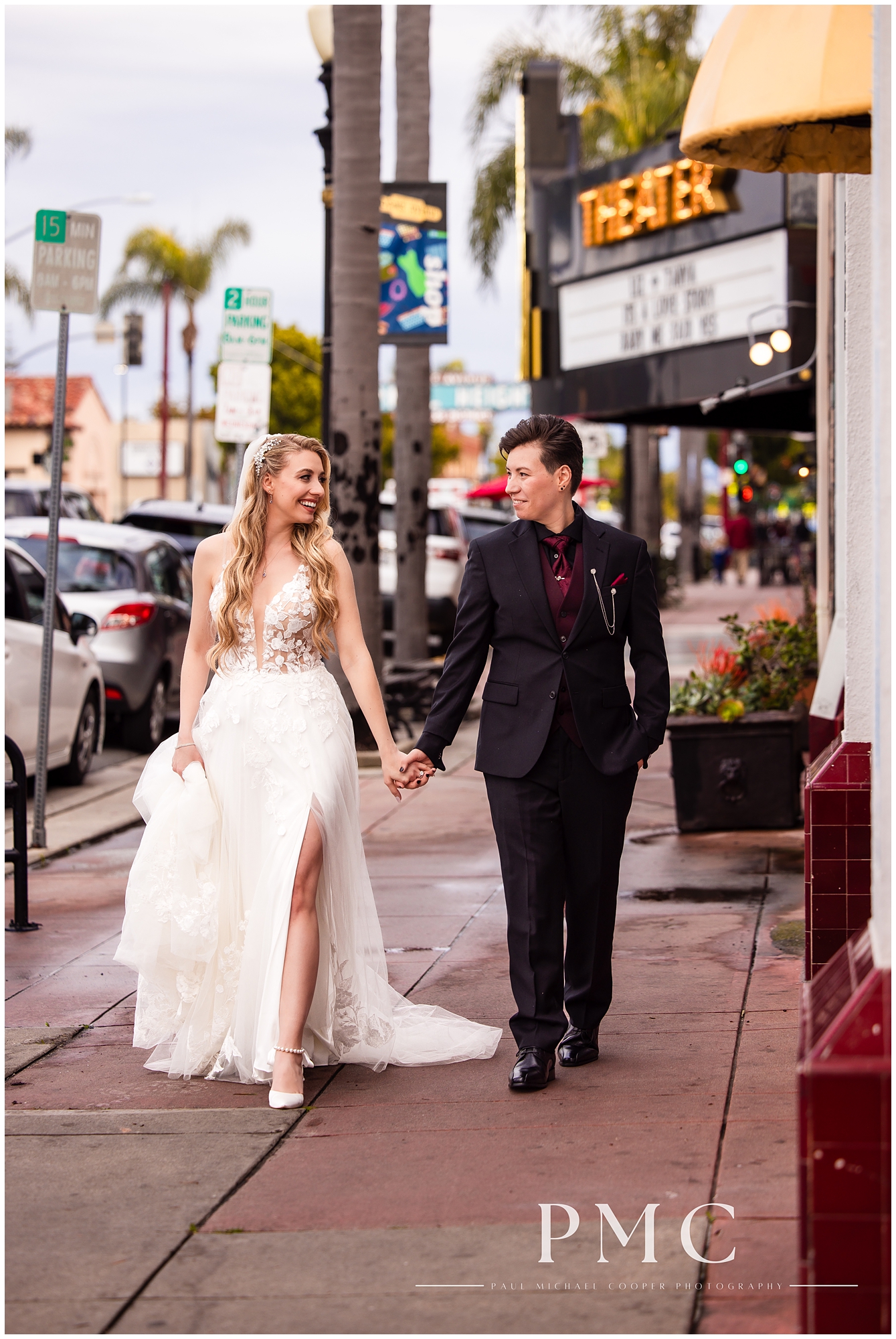 Two newlywed brides smile at each other while walking hand in hand down the sidewalk outside the Adams Avenue Theater, where they held their wedding.