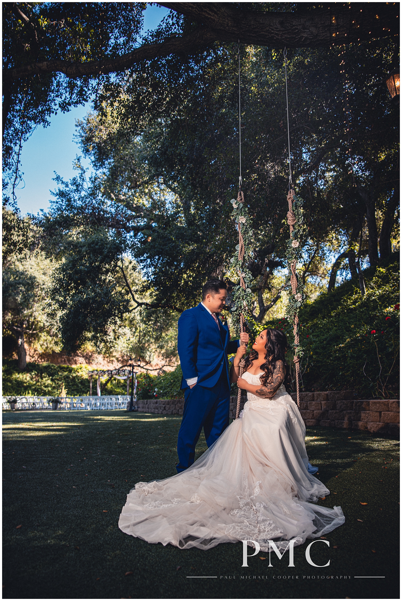 A bride seated on a rope swing looks up at her groom standing beside her among nature and greenery at Los Willows Wedding Venue in Fallbrook, Southern California.