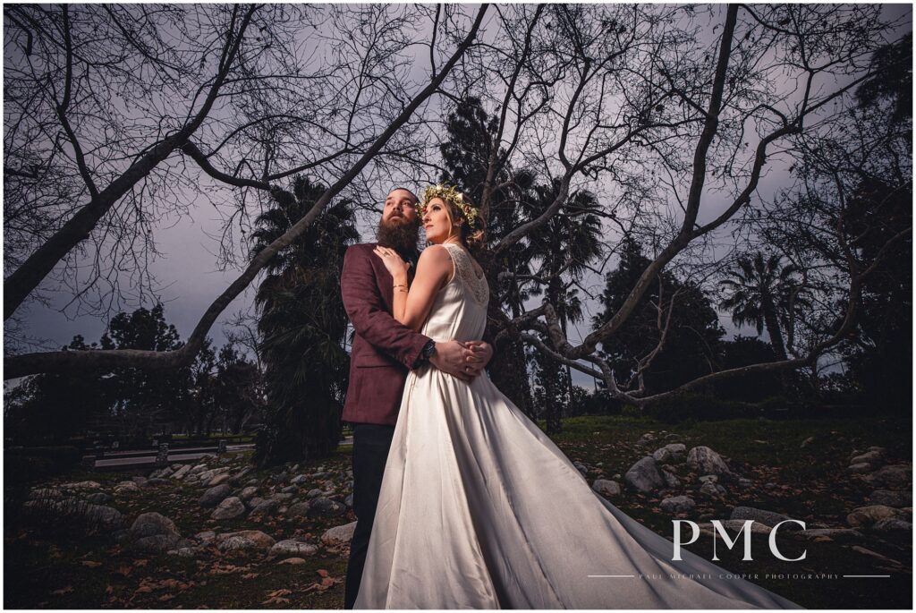 A bride and groom embrace in a dramatic, cinematic portrait among trees and nature on their boho wedding day, February 2024.