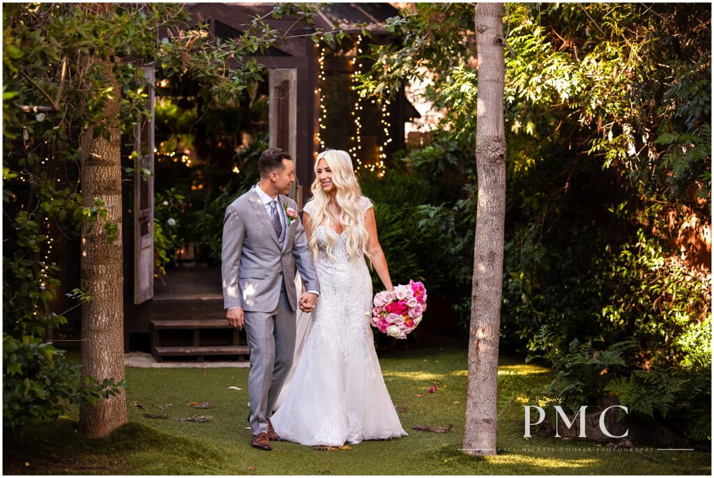 A bride and groom walk hand-in-hand through the verdant greenery at Twin Oaks Wedding Estate in San Marcos, Southern California.