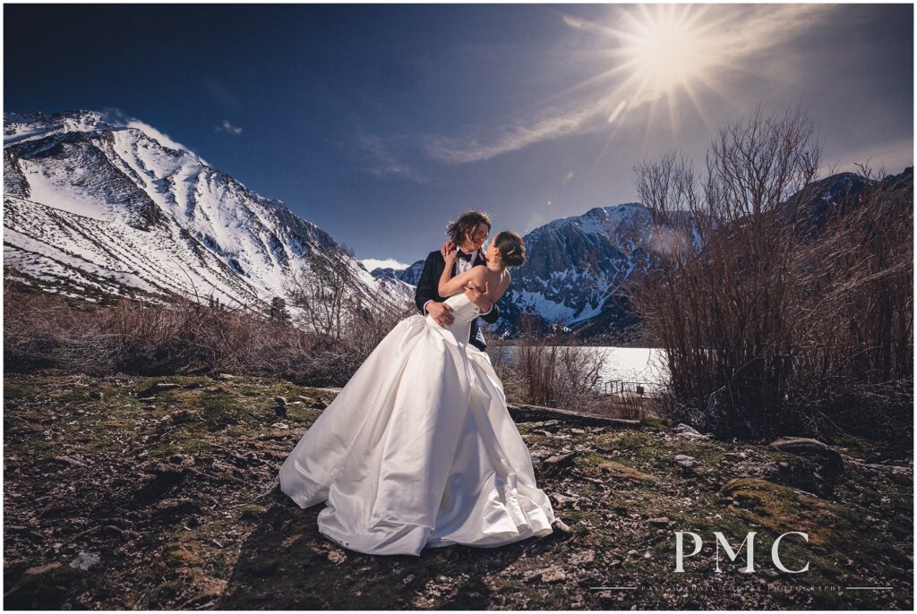 A bride and groom share a dramatic dip, surrounded by nature, on the shore of Convict Lake in Mammoth Lakes on their spring wedding day.