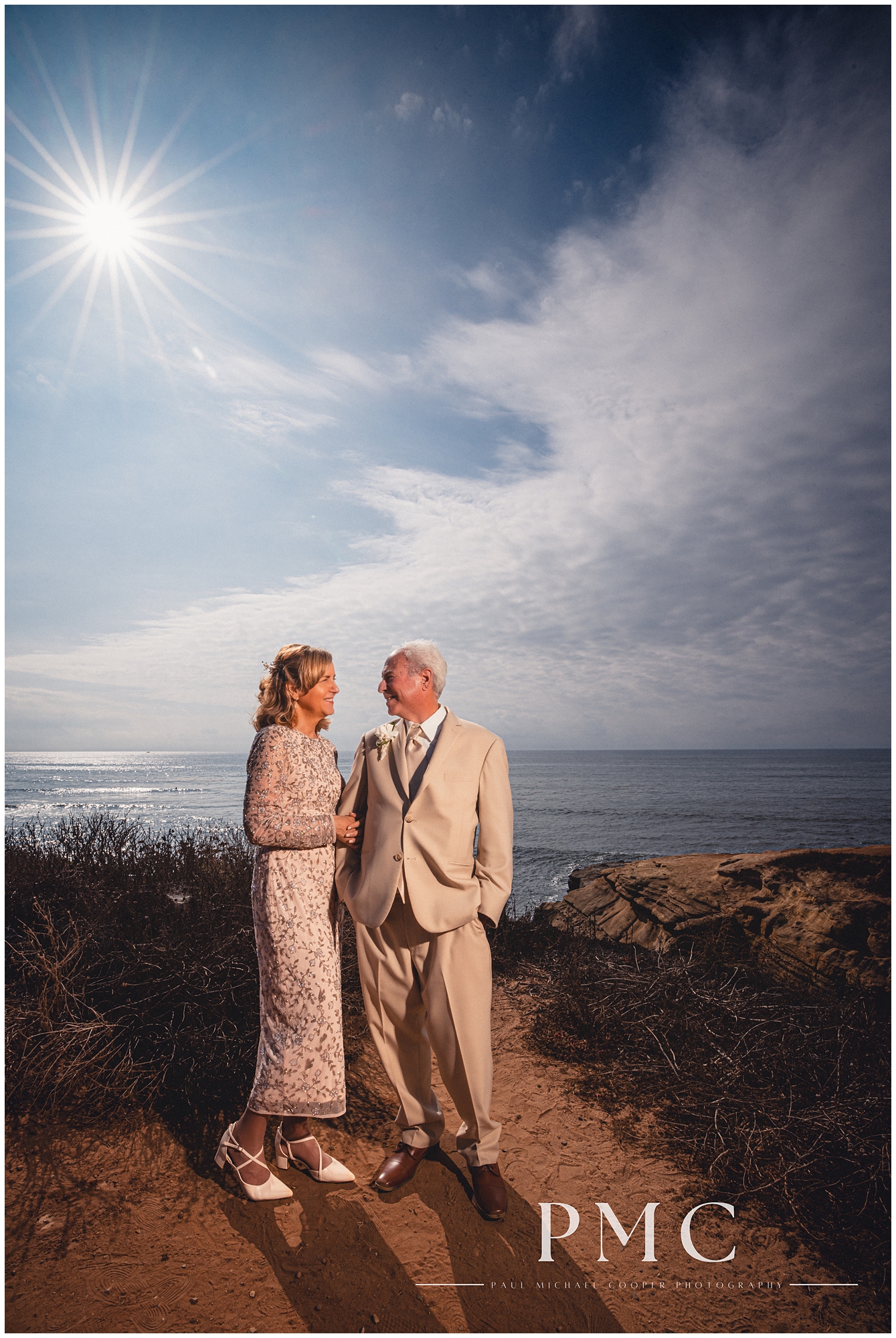 A bride and groom smile at each other after their small elopement on the shores of Sunset Cliffs, San Diego.