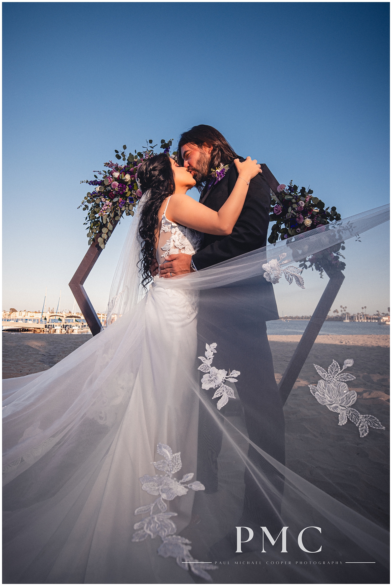 A bride and groom share a passionate kiss at the altar at their beach wedding in Mission Bay, summer 2024.