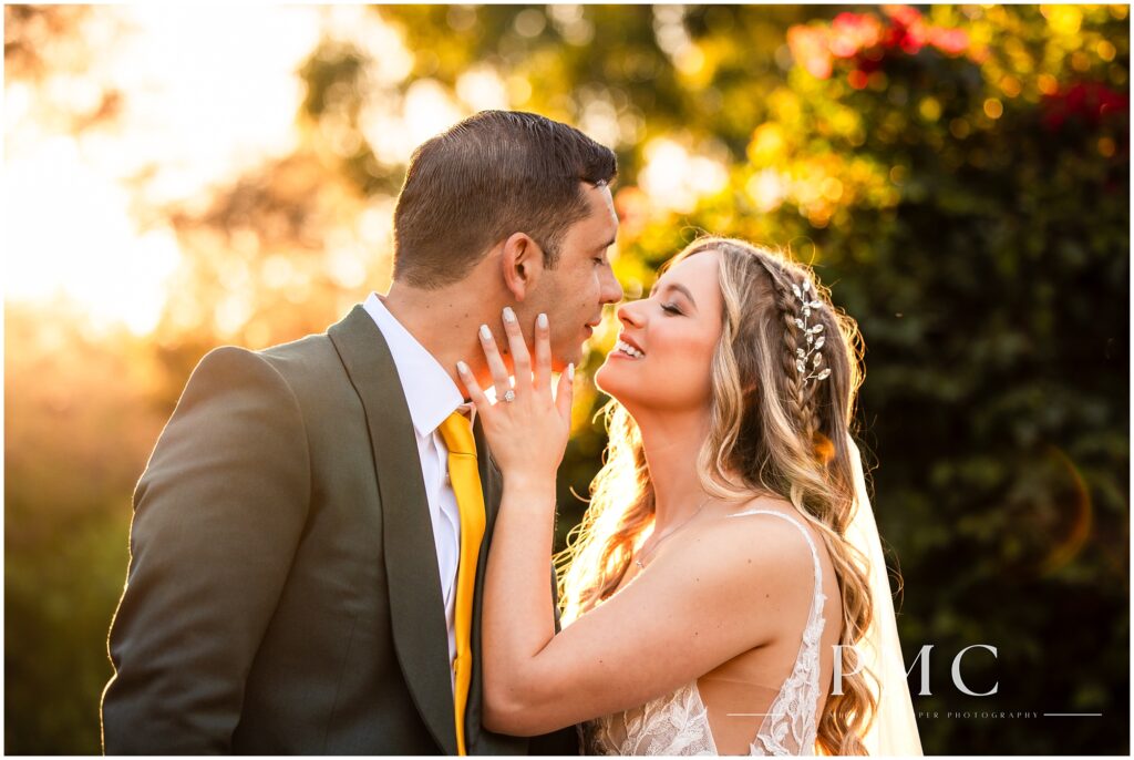 A bride and groom smile at each other as they lean in for a beautiful golden hour kiss on their wedding day.