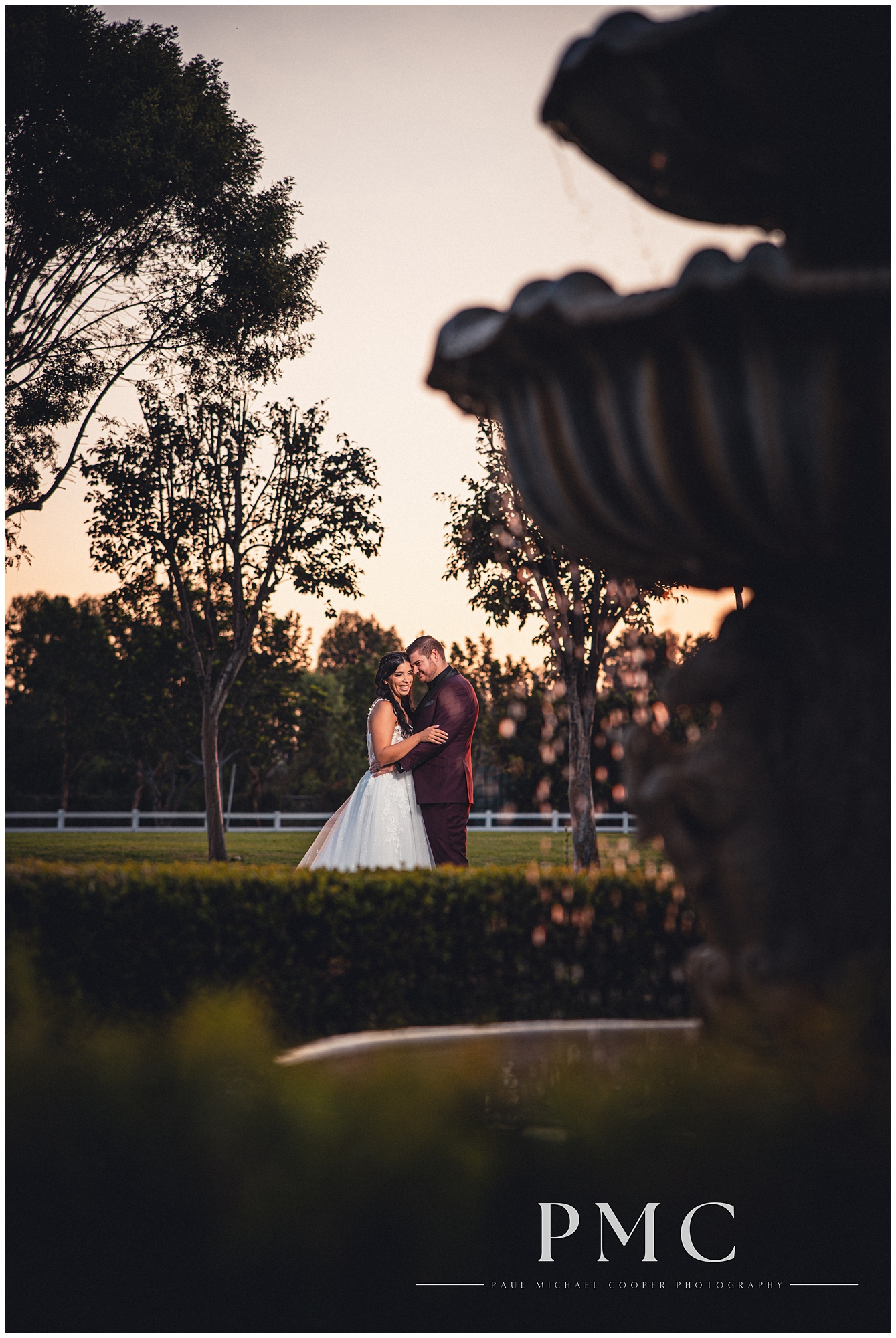 A bride and groom embrace and smile during golden hour by the fountain at the Farm in Norco on their summer wedding day.