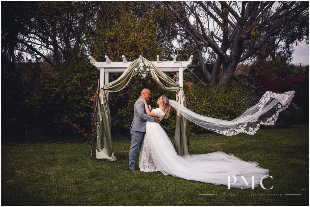 A bride and groom in a dramatic pose in front of the altar, with the bride's veil sweeping, on their Chula Vista wedding day.