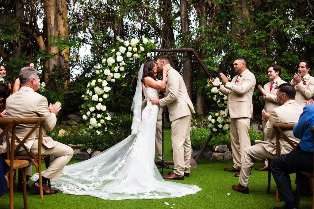 A bride and groom share their first kiss as married partners at the end of their wedding ceremony at Twin Oaks Wedding Estate in San Marcos. Photo by PMC Photography.