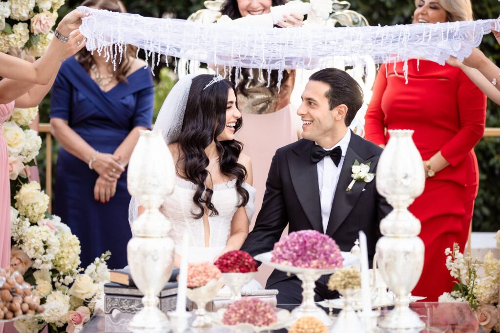 A Persian bride and groom laugh while seated at the Sofreh table during their wedding ceremony at the Westgate Hotel in Downtown San Diego. Photo by PMC Photography.