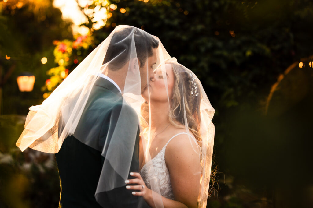 Newlywed bride and groom share a kiss under the bride's veil at sunset on their wedding day at Leo Carrillo Ranch, a wedding venue in Carlsbad belonging to Personal Touch Dining.