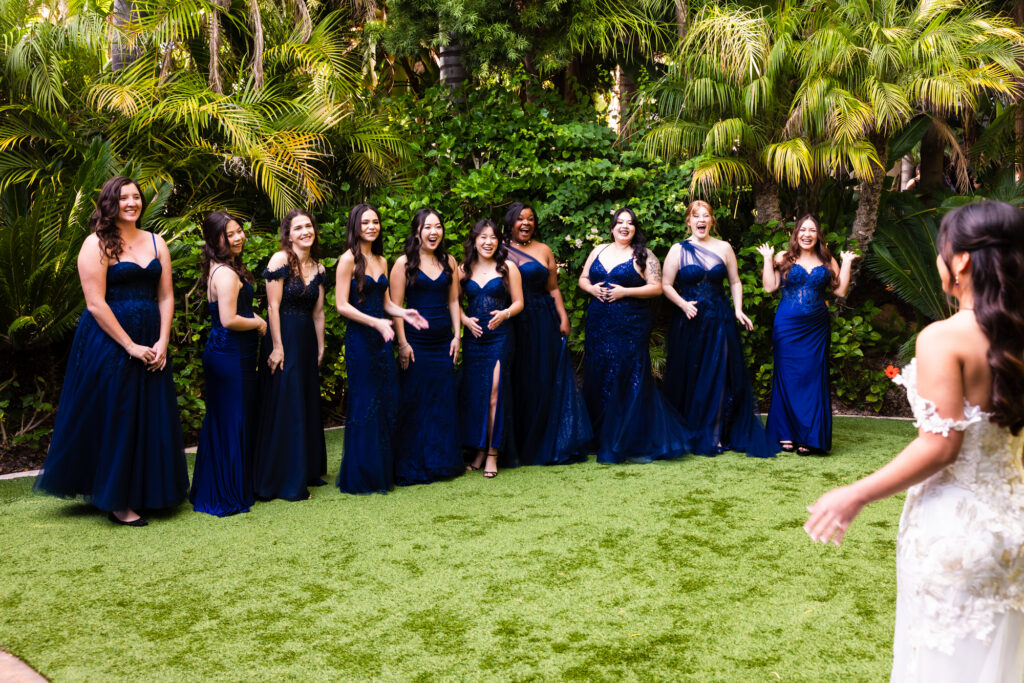 Bridesmaids in blue bridesmaids dresses smile and cheer at seeing the bride in her dress for the first time at Grand Tradition Estate and Gardens, a premier wedding venue in Fallbrook, Southern California.