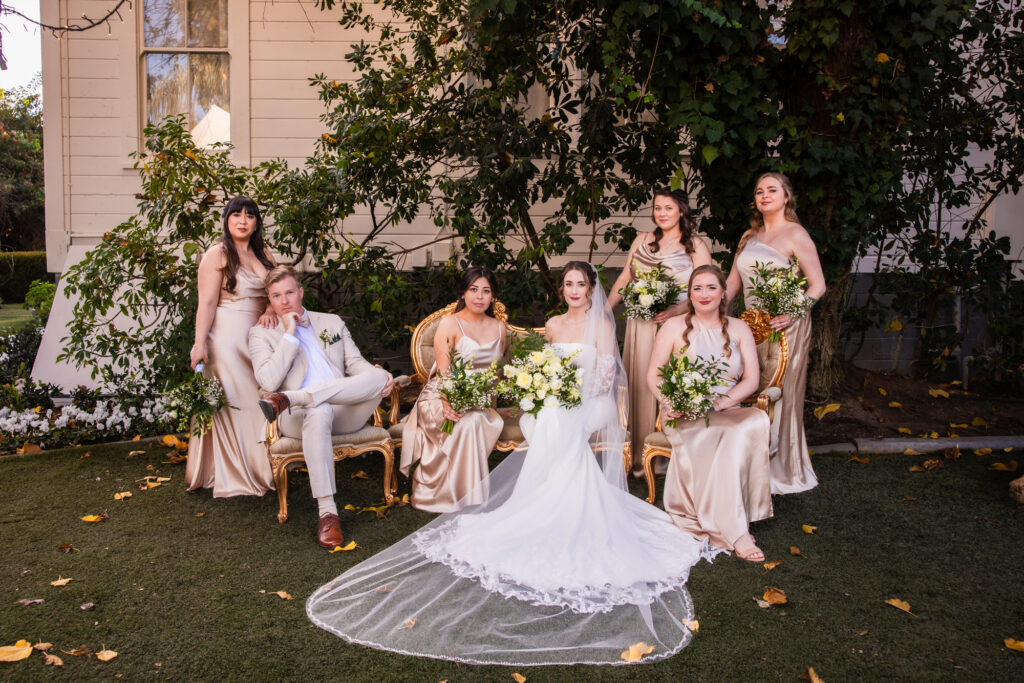 A bride and her bridesmaids, dressed in a champagne color, pose for the camera at Green Gables Wedding Estate, a wedding venue in San Diego, Southern California.