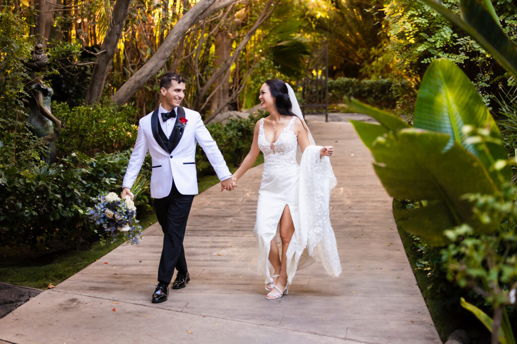Bride and groom laughing while walking hand in hand through the garden pathway at Botanica Oceanside wedding venue.