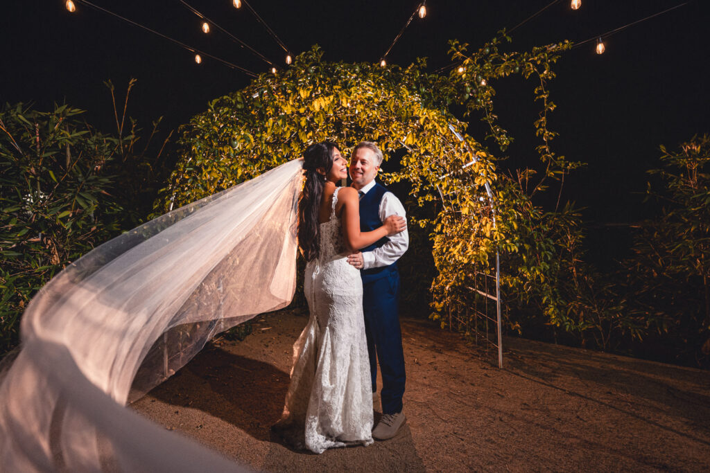 Bride and groom embracing under string lights at a Dia de los Muertos themed fall wedding in Vista, California.